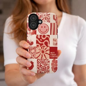 Op de afbeelding: Een telefoonhoesje met een patchwork-ontwerp in rood- en crèmetinten. De hoes heeft verschillende patronen, waaronder een smiley, bloemen en de tekst "BUT FIRST, COFFEE".