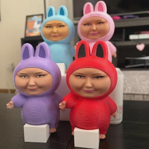 以下が含まれることがあります： 赤、紫、ピンク、青のバニーコスチュームを着た4体のカラフルなフィギュア。各フィギュアは小さな白いブロックの上に立っています。フィギュアは笑顔です。