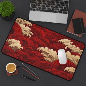 May include: A rectangular desk mat featuring a Japanese wave pattern in shades of red and cream. The mat has a black border and is designed to accommodate a computer mouse and keyboard. A white mouse is visible on the mat.