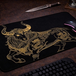 Peut inclure: Tapis de souris rectangulaire noir avec une illustration dorée d'un taureau et d'un dragon. Une souris noire avec des lumières roses et blanches est posée dessus. Un clavier, un casque et un appareil photo sont également visibles.