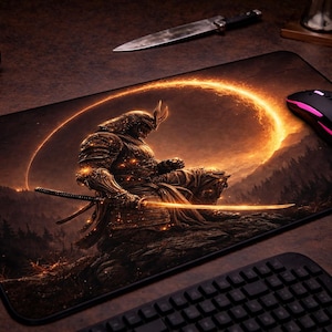 Puede incluir: Alfombrilla de ratón rectangular con una ilustración detallada de un guerrero samurái con armadura dorada, sosteniendo una katana. El diseño incluye un arco naranja brillante y un fondo oscuro y montañoso. Un ratón negro con detalles rosas está encima.