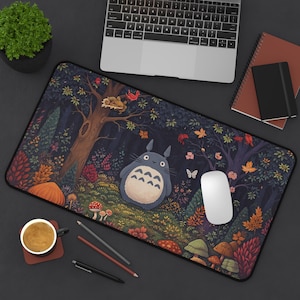 May include: A rectangular mousepad featuring a whimsical forest scene with a large, blue, cartoon-like character. The design includes trees, mushrooms, and colorful foliage. A laptop, mouse, and other desk items are visible.