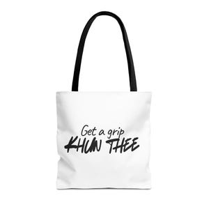 May include: A white tote bag with black handles featuring the black text Get a grip KHUN THEE printed on the front. The bag has a rectangular shape with a flat bottom and a simple design, showcasing bold lettering against a plain white background.