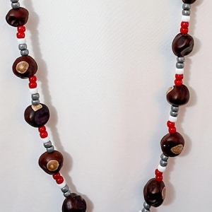 May include: A handmade necklace featuring large, dark brown beads interspersed with red, white, and silver beads. The necklace is strung on a red cord, creating a striking contrast.
