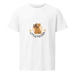 May include: White t-shirt featuring a cartoon dog illustration in brown and tan, with the text "LITTLE FECKER" in black. The design includes a light orange circle and star accents.