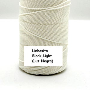 May include: A spool of off-white Linhasita Black Light cord. The label on the spool reads "Linhasita Black Light (Luz Negra)". The cord is tightly wound around a cardboard core. The cord appears to be made of a durable, woven material.