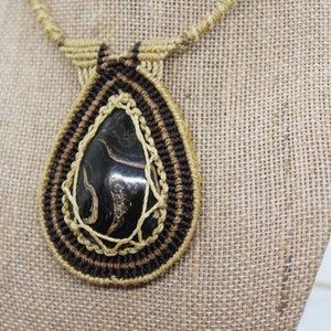 May include: A black and gold macrame necklace with a teardrop-shaped stone pendant.