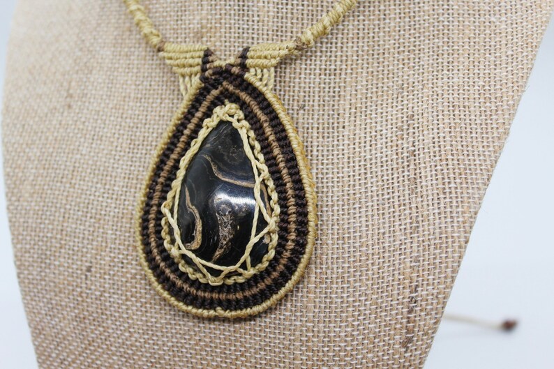 May include: A black and gold macrame necklace with a teardrop-shaped stone pendant.