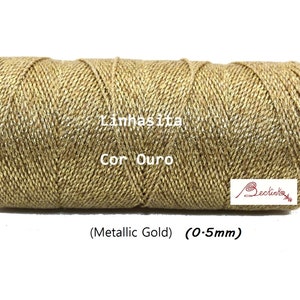 May include: A spool of metallic gold thread, labeled "Linhas Ita Cor Ouro (Metallic Gold) (0.5mm)".