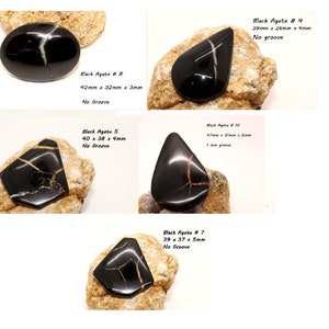 Puede incluir: Cinco cabujones de ágata negra con vetas blancas y doradas. Los cabujones son de formas y tamaños variados, que van desde los 37 hasta los 97 milímetros de longitud. Los cabujones están sobre una superficie rocosa. Ágata negra n.º 8, 42 mm x 32 mm x 3 mm, sin ranura. Ágata negra 5, 40 x 38 x 4 mm, sin ranura. Ágata negra n.º 10, 97 mm x 31 mm x 5 mm, ranura de 1 mm. Ágata negra n.º 7, 39 x 37 x 5 mm, sin ranura. Ágata negra n.º 4, 39 mm x 26 mm x 4 mm, sin ranura.
