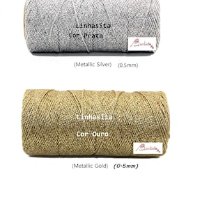 May include: Two spools of metallic thread, one silver and one gold. The spools are labeled "Linhasita Cor Prata" and "Linhasita Cor Ouro". Both spools are 0.5 mm thick.