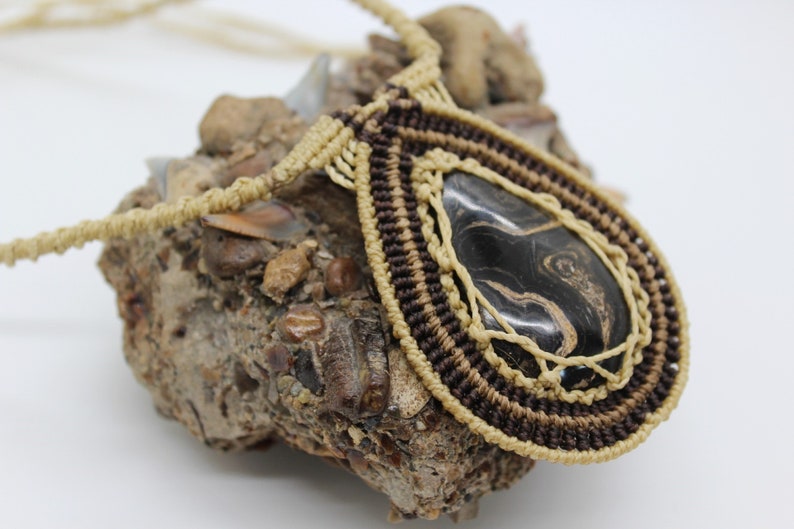 May include: A black and gold stone pendant necklace with a macrame design. The pendant is a teardrop shape and the stone has a swirling pattern.