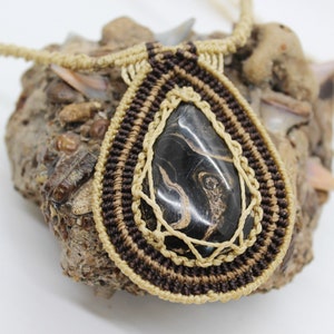May include: A brown and beige macrame necklace with a black and gold agate pendant.