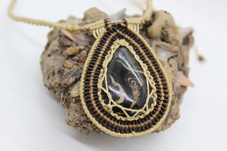 May include: A brown and beige macrame necklace with a black and gold agate pendant.