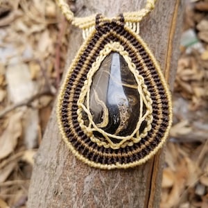 May include: A brown and beige macrame necklace with a black and gold stone pendant.