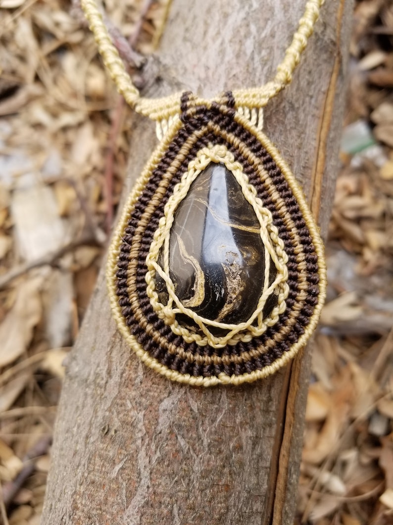 May include: A brown and beige macrame necklace with a black and gold stone pendant.