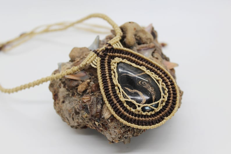 May include: A brown and beige macrame necklace with a black and gold agate pendant.
