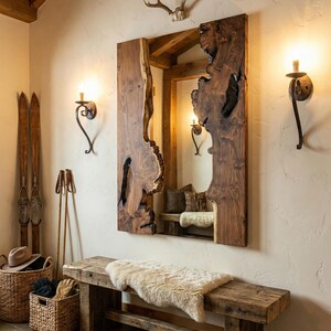 May include: A large, rustic wooden mirror with a live edge, mounted on a cream-colored wall. The mirror reflects a cozy interior with a bench, pillows, and a sheepskin rug. The room is decorated with vintage skis, a basket, and sconces.