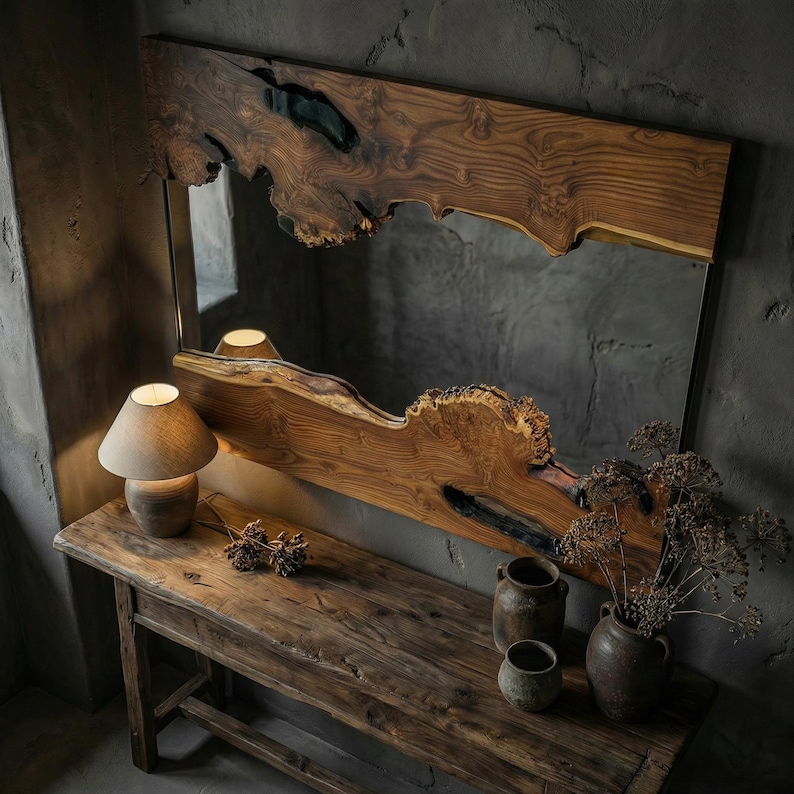 May include: A large, rectangular mirror with a live edge wooden frame. The frame is a warm brown color with a natural, organic shape. The mirror hangs above a rustic wooden console table, with a small lamp and pottery.