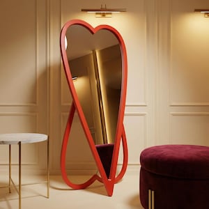May include: A large, red, heart-shaped floor mirror. The mirror has a sleek, modern design with a continuous frame. The mirror is approximately 183 cm tall. The mirror is a decorative accent piece for a bedroom or living space.