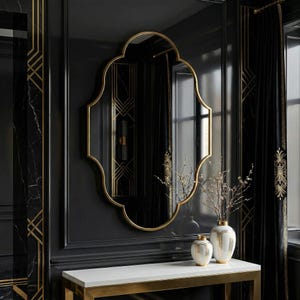 May include: A large, ornate mirror with a gold frame hangs on a black wall. The mirror has a unique, scalloped shape. Below the mirror is a white table with gold trim, and two white vases with gold accents. Black curtains with gold trim are on the right.