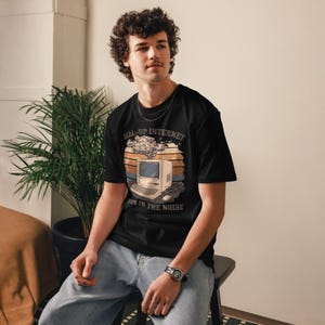 Könnte beinhalten: Schwarzes T-Shirt mit einem Retro-Computer-Grafik und dem Text "DIAL-UP INTERNET BORN IN THE NOISE". Das Design zeigt einen Vintage-Computer mit einer Datenwolke darüber, vor einem Sonnenuntergangshintergrund.