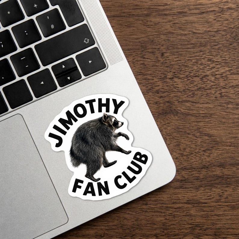 May include: A die-cut sticker featuring a realistic illustration of a gray and black raccoon in a walking pose, surrounded by the bold black text JIMOTHY FAN CLUB arranged in a circular arc on a white background.
