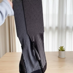 May include: Dark gray tights with a subtle polka dot pattern. The tights are held up, showcasing their full length and design. The fabric appears soft and stretchy, with a solid black band at the top and bottom.