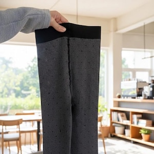 May include: Dark gray leggings with a black waistband and a dotted pattern are held up by a person. The leggings are made of a soft material and appear to be warm. The background is a bright room with wooden furniture.
