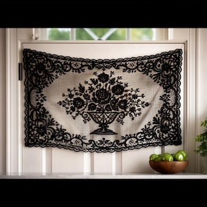 May include: Black lace curtain with a floral design. The curtain is rectangular with a scalloped edge and a central motif of flowers in a vase. The curtain is hanging on a white door.