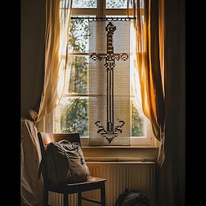 May include: A woven sword-shaped window decoration hangs in front of a window with sheer curtains. A backpack rests on a wooden chair. The window looks out onto a garden, with sunlight streaming through.