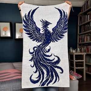 May include: A rectangular crochet tapestry featuring a white background with a large, detailed dark blue phoenix bird design. The mythical bird is depicted with expansive, feathered wings spread wide and a long, flowing tail that curls downwards.