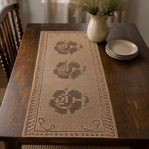 May include: A rectangular beige crochet table runner featuring a repeating pattern of three dark brown rose motifs. The runner has a delicate openwork grid design with a decorative border and is centered on a dark wood table surface.