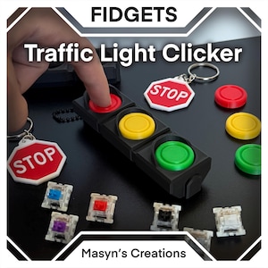 May include: A black traffic light clicker with red, yellow, and green buttons. The image also shows a stop sign keychain and individual colored buttons. The text on the image reads "FIDGETS" and "Traffic Light Clicker".