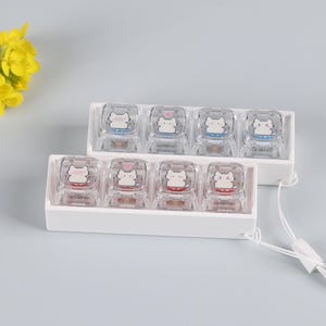 Può includere: Due set di tasti per tastiera quadrati e trasparenti con un design a gatto dei cartoni animati. Ogni tasto ha un gatto bianco con un cuore. Un set ha accenti blu, l'altro rossi. I tasti sono in vassoi di plastica bianca.