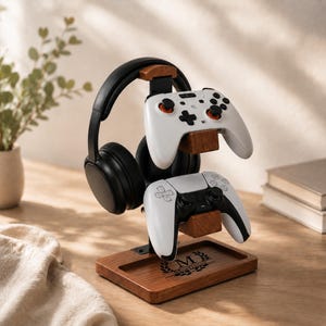 Könnte beinhalten: Ein Gaming-Ständer aus Holz und schwarzem Metall mit einer Basis, die mit dem Buchstaben M und dem Namen Mortimer graviert ist, und zwei weiße Gamecontroller mit schwarzen und orangefarbenen Akzenten an den Joysticks hält.