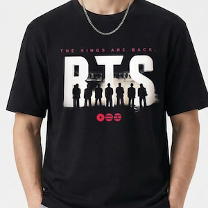 May include: Black t-shirt with the text "BTS" in large white letters. Below the text is a silhouette of seven figures and three red circles. Above the text is the phrase "THE KINGS ARE BACK."