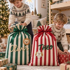May include: Two large fabric gift sacks with drawstring closures and satin ribbons. One sack features green and white vertical stripes with a lion patch and the name Oliver. The other has red and white stripes with a dog patch and the name Theo.