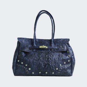 Può includere: Una borsa a mano blu scuro con finitura testurizzata e stropicciata, dotata di due manici, una chiusura a girello in metallo argentato su un cinturino orizzontale e borchie decorative in metallo argentato disposte ad arco sulla base.