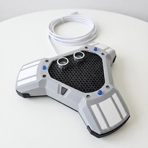 May include: A gray and black microphone with a mesh center, two silver circular components, and a white cord. The microphone has blue lights and white rectangular accents. The device is on a white surface.