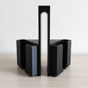 May include: Black metal bookends with a modern design. The bookends have a rectangular base with a vertical support and a curved cutout. The bookends are on a light wood surface.