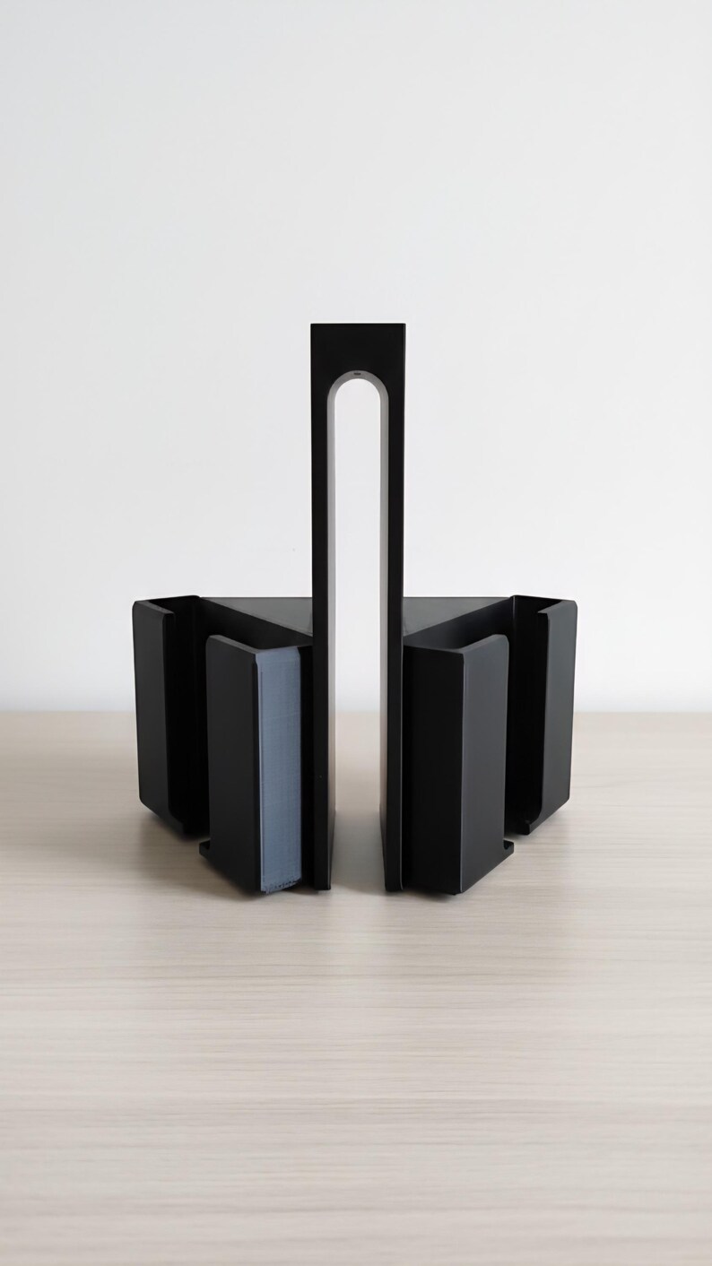 May include: Black metal bookends with a modern design. The bookends have a rectangular base with a vertical support and a curved cutout. The bookends are on a light wood surface.