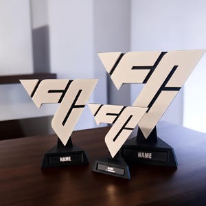 May include: Three awards with a white and black geometric design. Each award features a white, V-shaped top with black accents, set on a black base. The base of each award has the word "NAME" printed on it.