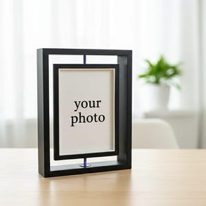 May include: A black double-frame photo holder with the text "your photo" on a white background. The frame has a rectangular design with a smaller inner frame. The photo holder is on a light-colored wooden surface.