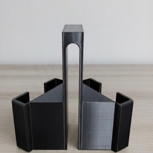 May include: Black geometric bookends. The bookends have a modern design with a rectangular base and a tall, arched support. The bookends are made of a solid, matte black material and are displayed on a light wood surface.