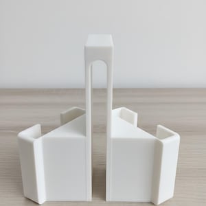May include: Two white, geometric bookends. Each bookend has a rectangular base with a sloped top and a curved, vertical handle. The bookends are made of a solid, opaque material and are designed to hold books upright.