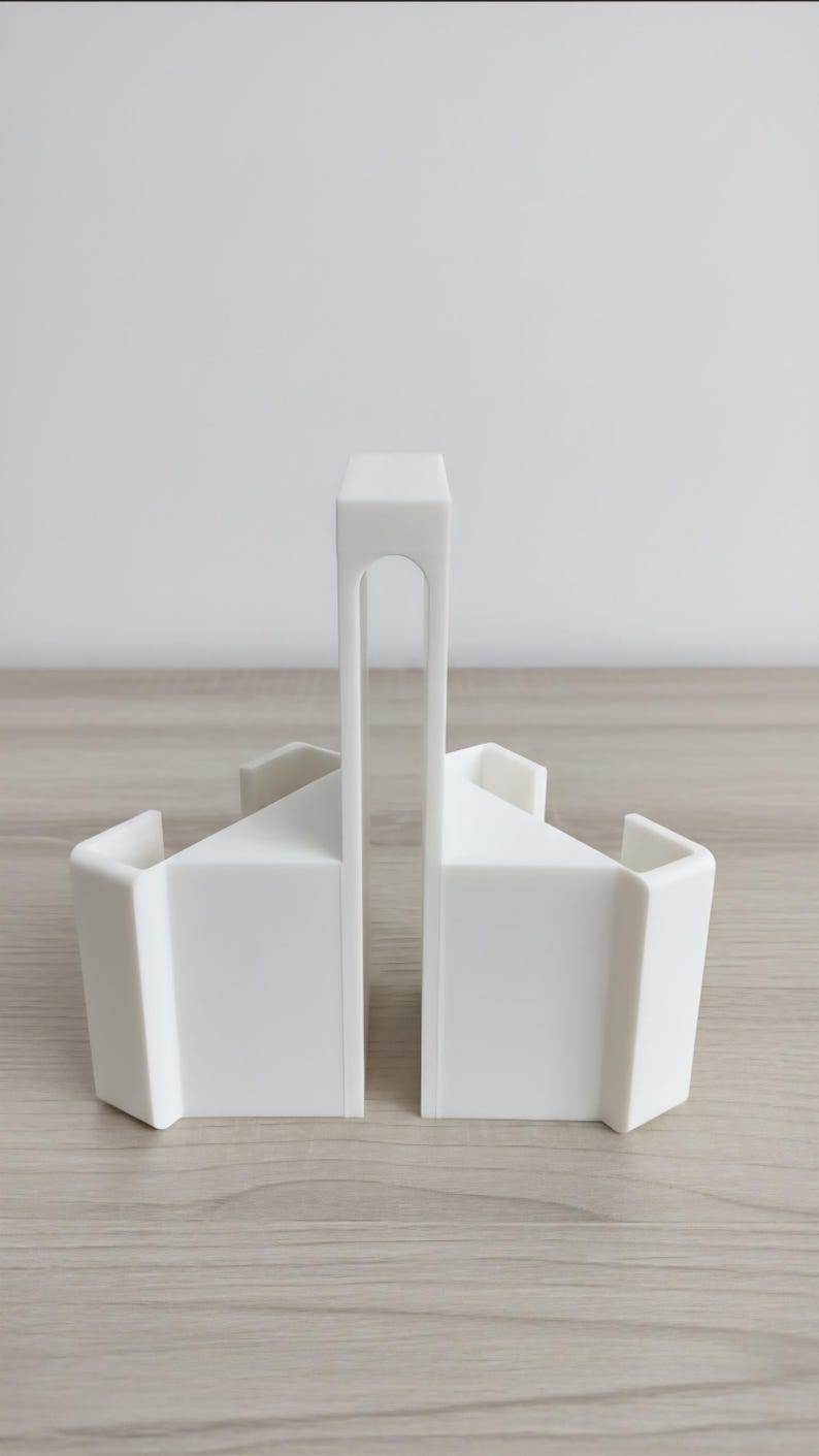 May include: Two white, geometric bookends. Each bookend has a rectangular base with a sloped top and a curved, vertical handle. The bookends are made of a solid, opaque material and are designed to hold books upright.