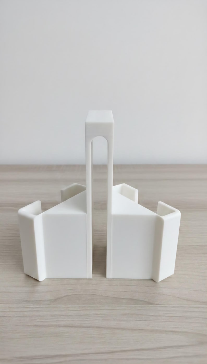 May include: Two white bookends with a minimalist design. Each bookend has a rectangular base and a triangular top, connected by a vertical support with an arched cutout. The bookends are made of a solid, opaque material.