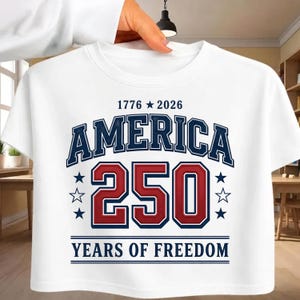 May include: A white t-shirt featuring a graphic design with the text 1776 star 2026 at the top, the word AMERICA in dark blue, the number 250 in large red digits, and the text YEARS OF FREEDOM at the bottom, accented by dark blue and white stars.