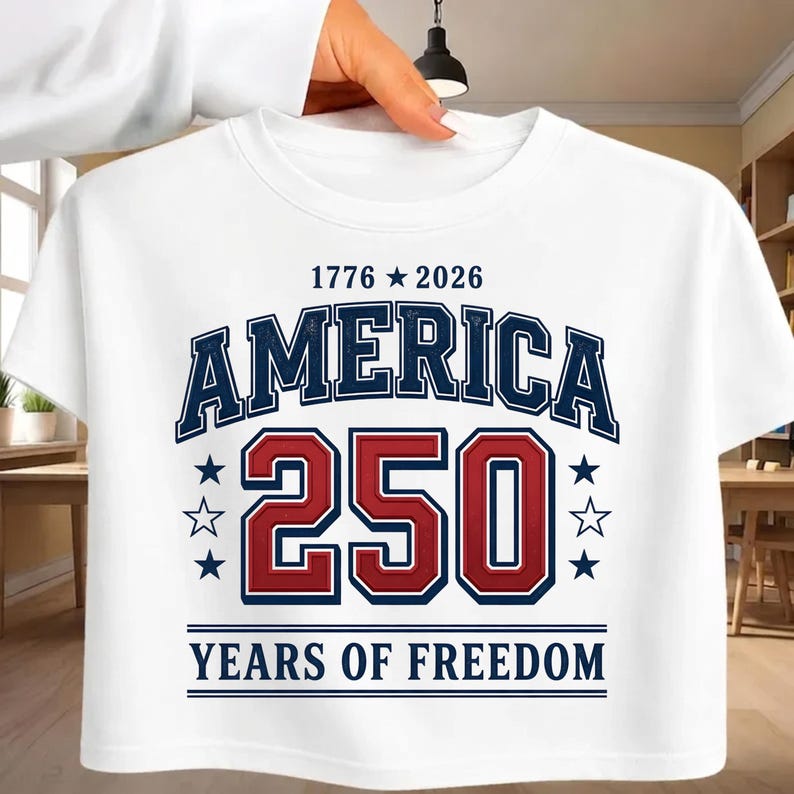 May include: A white t-shirt featuring a graphic design with the text 1776 star 2026 at the top, the word AMERICA in dark blue, the number 250 in large red digits, and the text YEARS OF FREEDOM at the bottom, accented by dark blue and white stars.